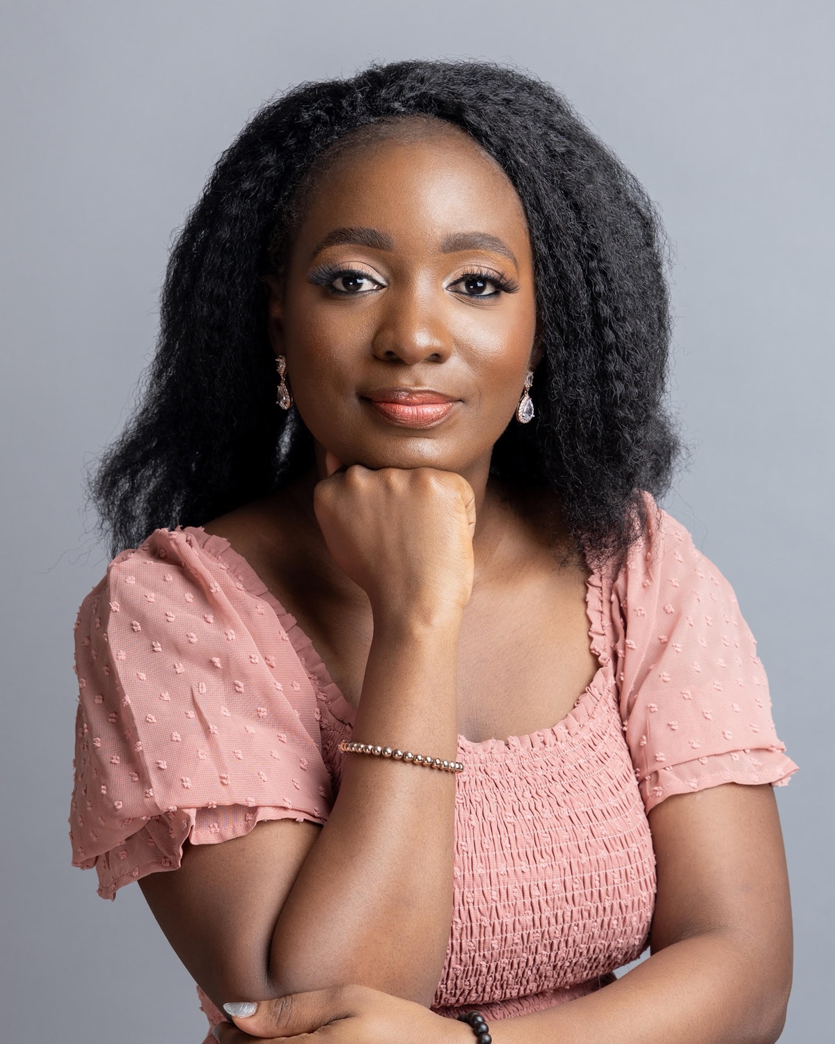 Abimbola Olumuyiwa smiling, chin resting on her hand, wearing a pink dress